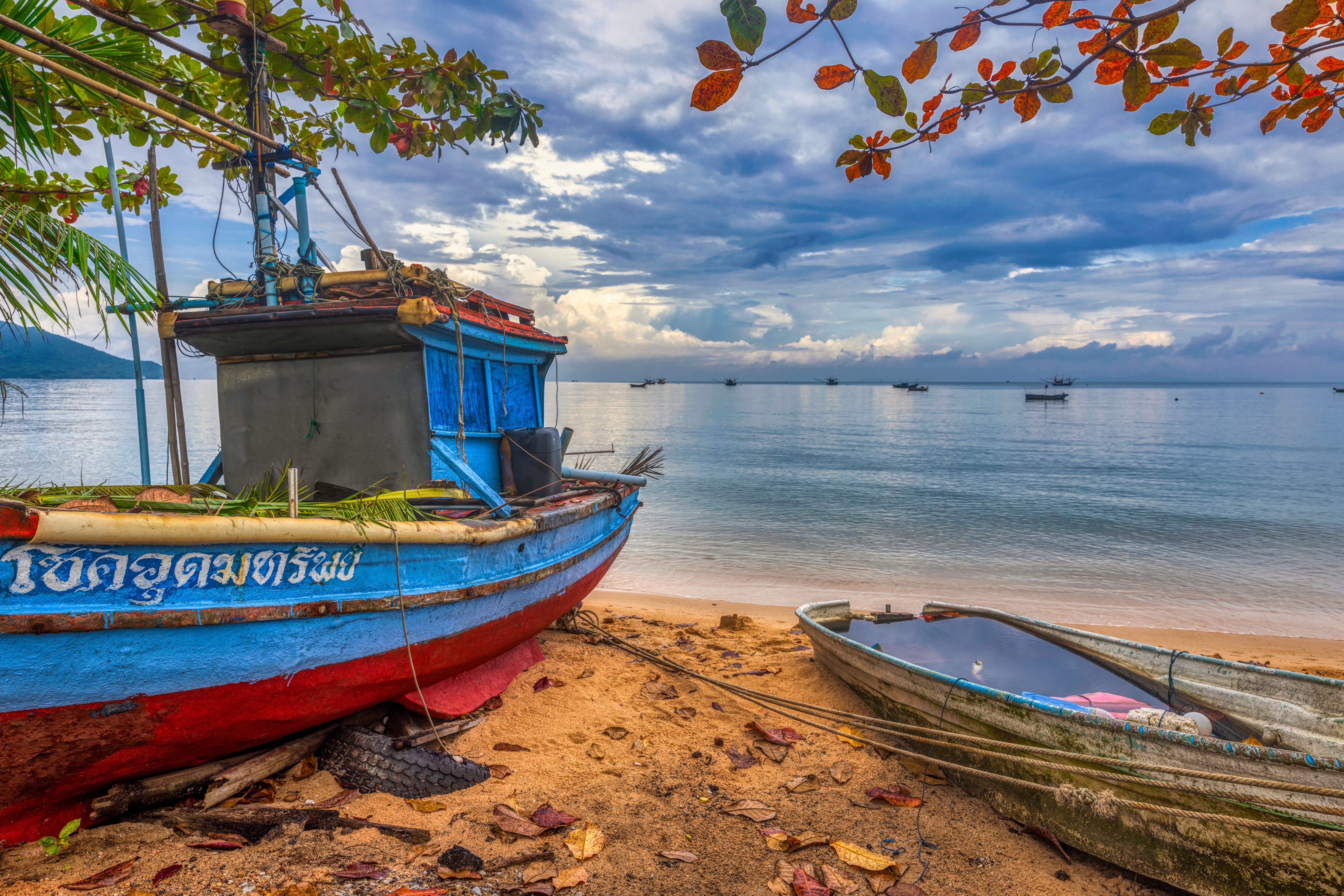 Wooden fishing boats pulled up on the sand at Bang Saen beach under a cloudy upper-Gulf sky
