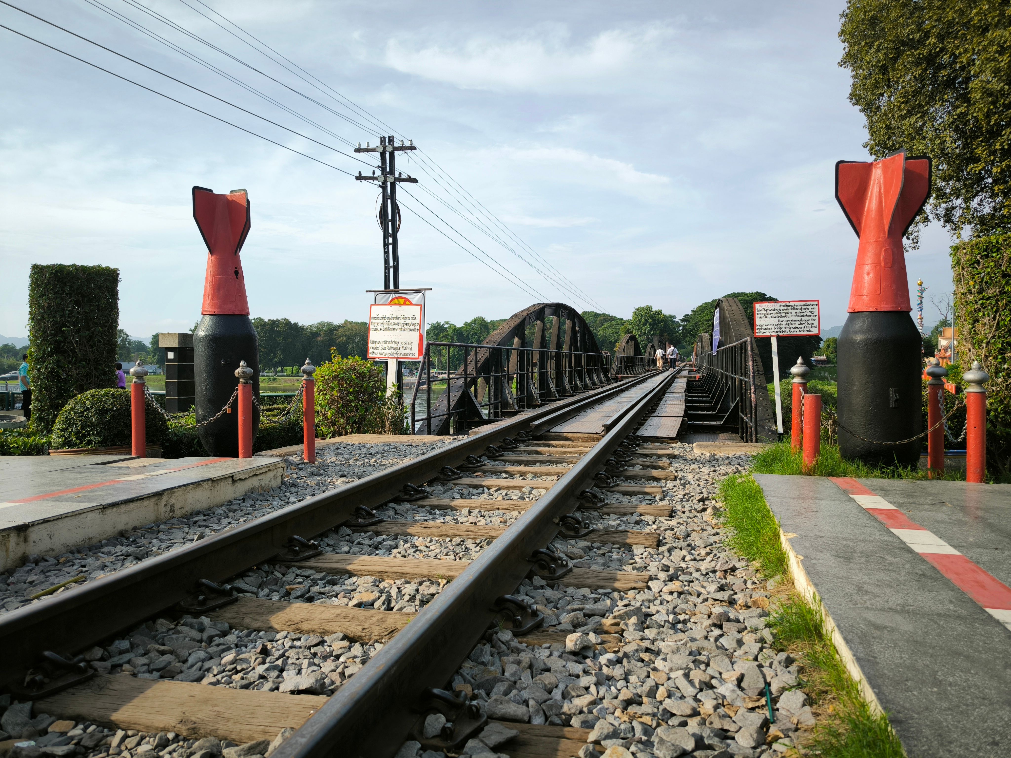The railway track crossing the steel Bridge over the River Kwai at Kanchanaburi, red bomb-shaped markers flanking the near end