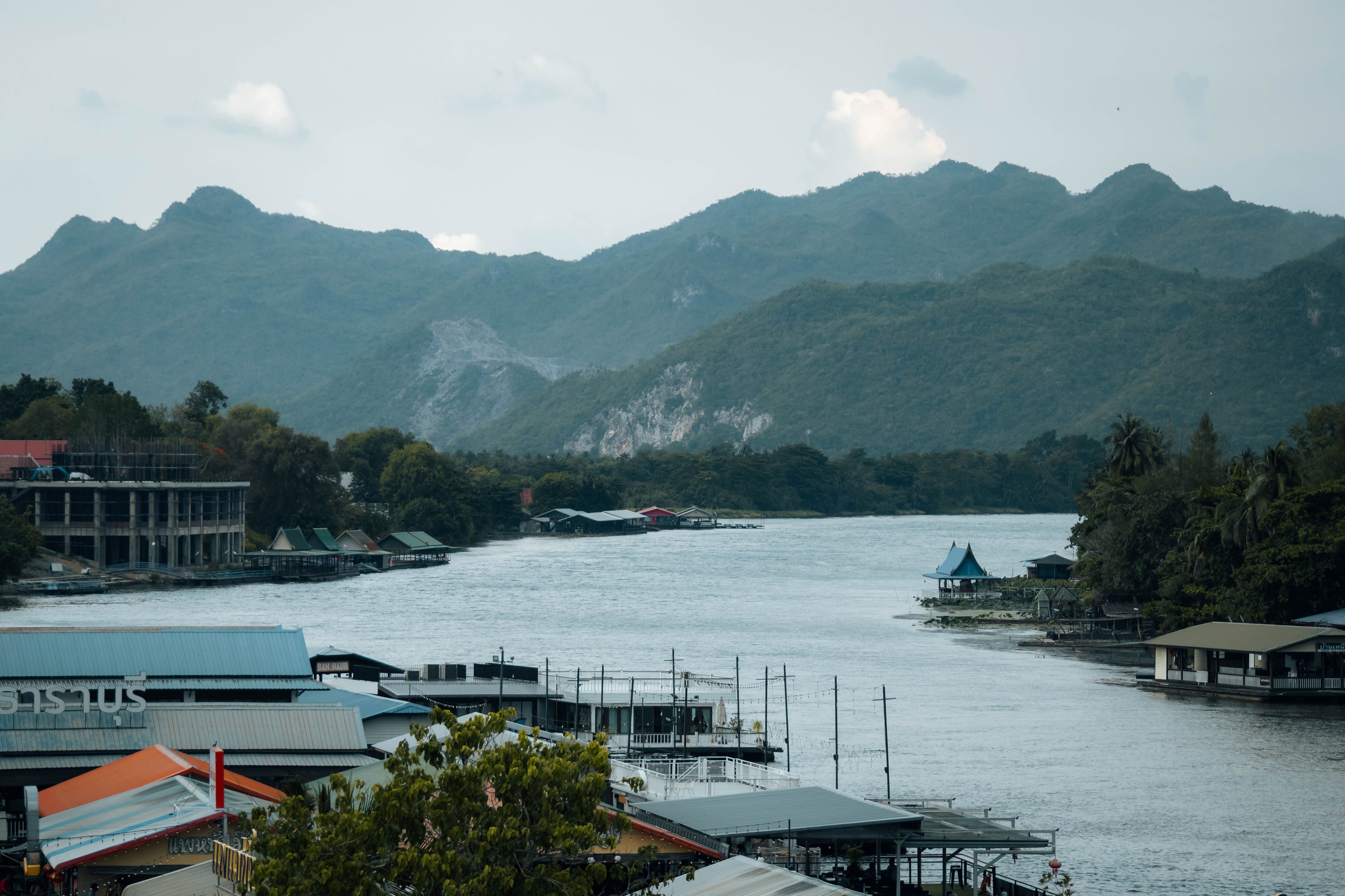 Floating raft houses and restaurants lining the River Kwai at Kanchanaburi, with forested hills rising behind